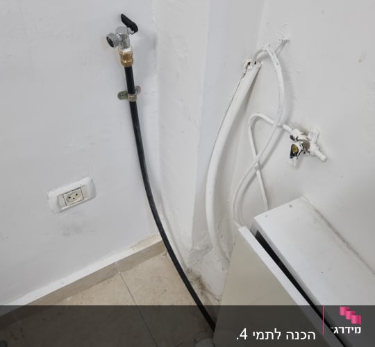 ברז מים מחובר לצינור שחור על קיר לבן